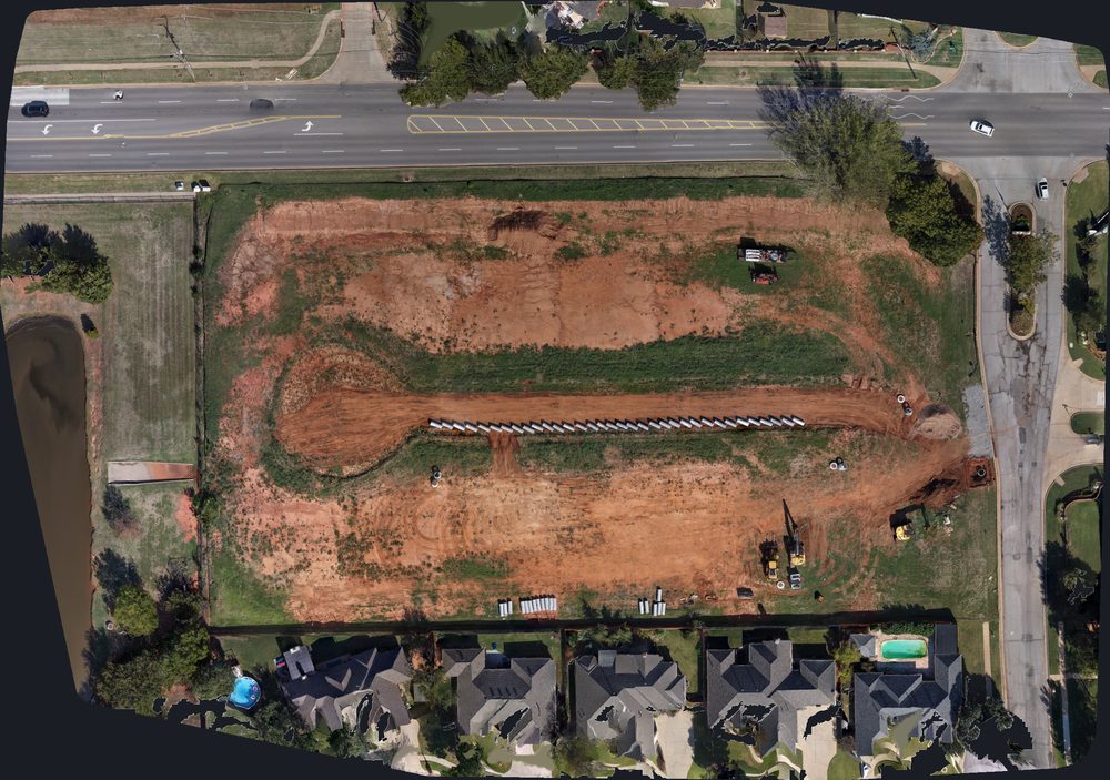 Top-down drone orthomosaic of a graded development site with a storm pipe trench and equipment